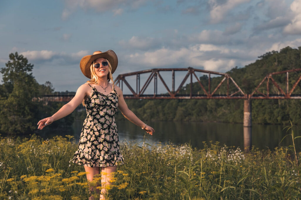 A Hardin, Valley Academy high school student in front of a train Trussell that goes over a river. She is wearing a cowboy hat.